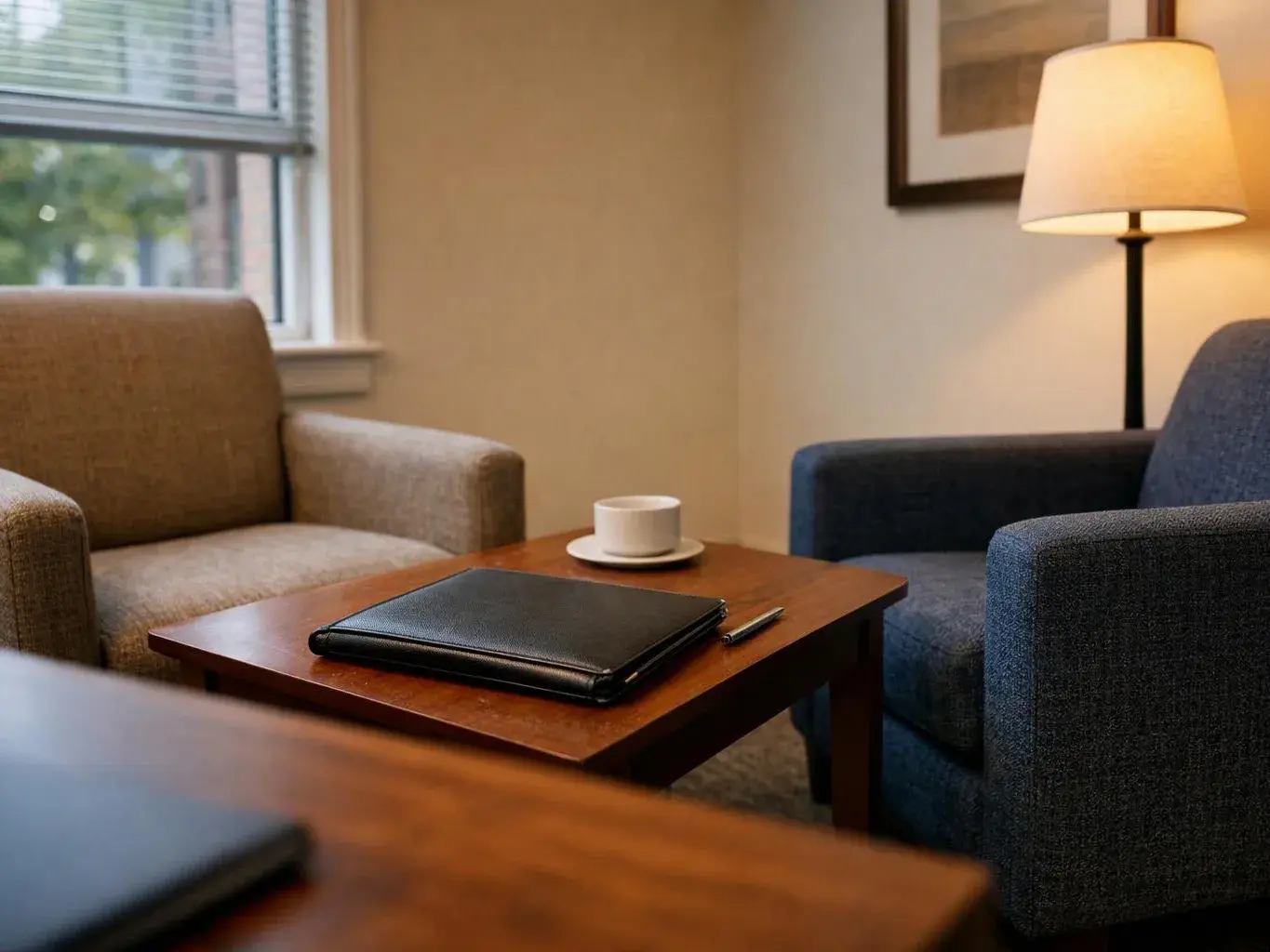 A cozy lounge shows two armchairs, a lamp, and a coffee table with a notebook, pen, and cup
