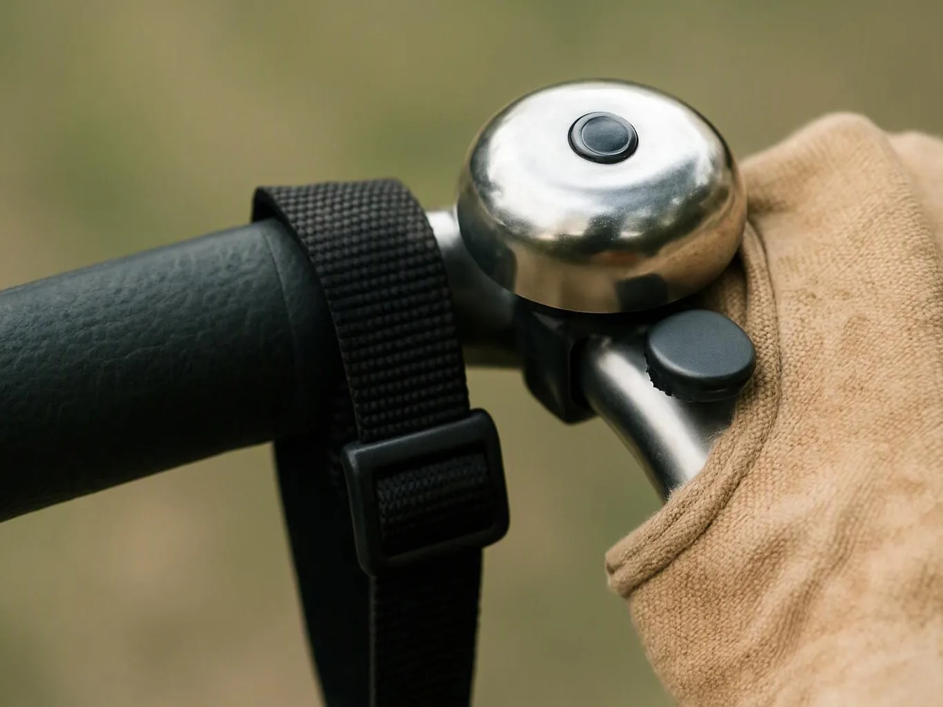 A gloved hand grips a bicycle handlebar beside a silver bell and black strap