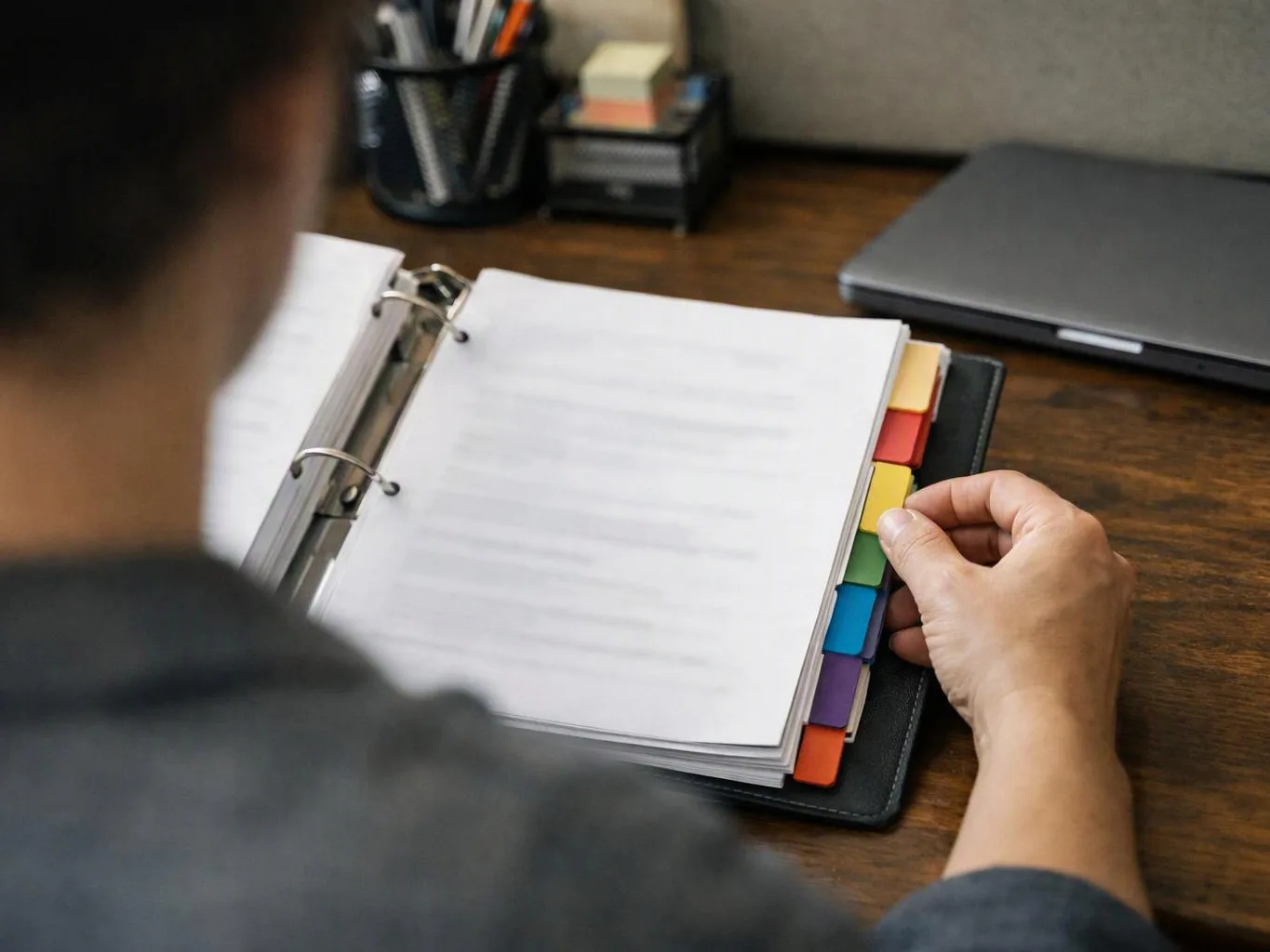A person flips through a ring binder with colored tabs at a wooden desk
