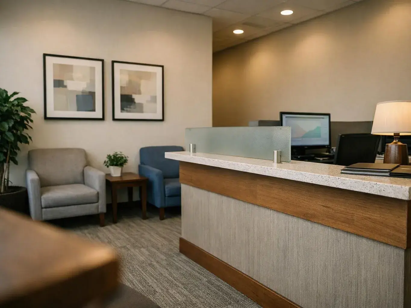 A quiet office waiting area shows a reception desk, two chairs, framed wall art, and a lamp